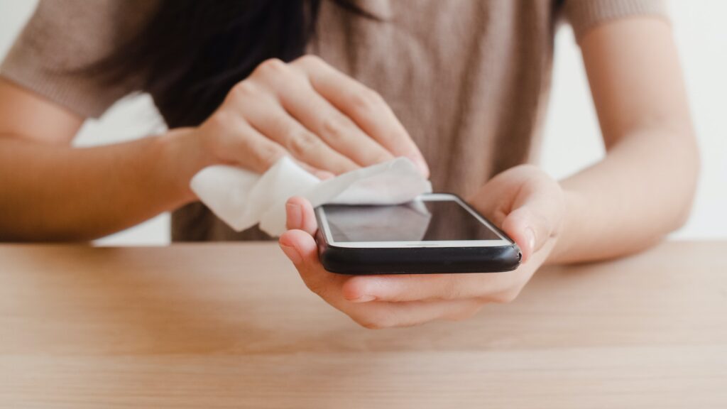 Asian woman using alcohol spray on tissue clean mobile phone before use it for protect coronavirus.