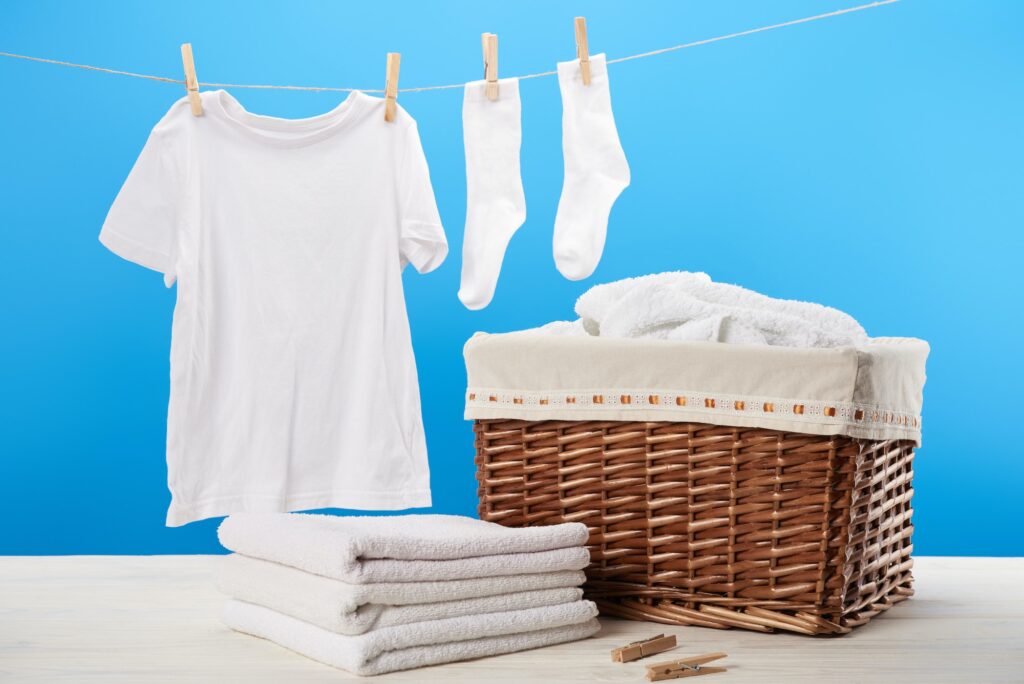 laundry basket, pile of clean soft towels and white clothes hanging on clothesline on blue