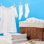 laundry basket, pile of clean soft towels and white clothes hanging on clothesline on blue