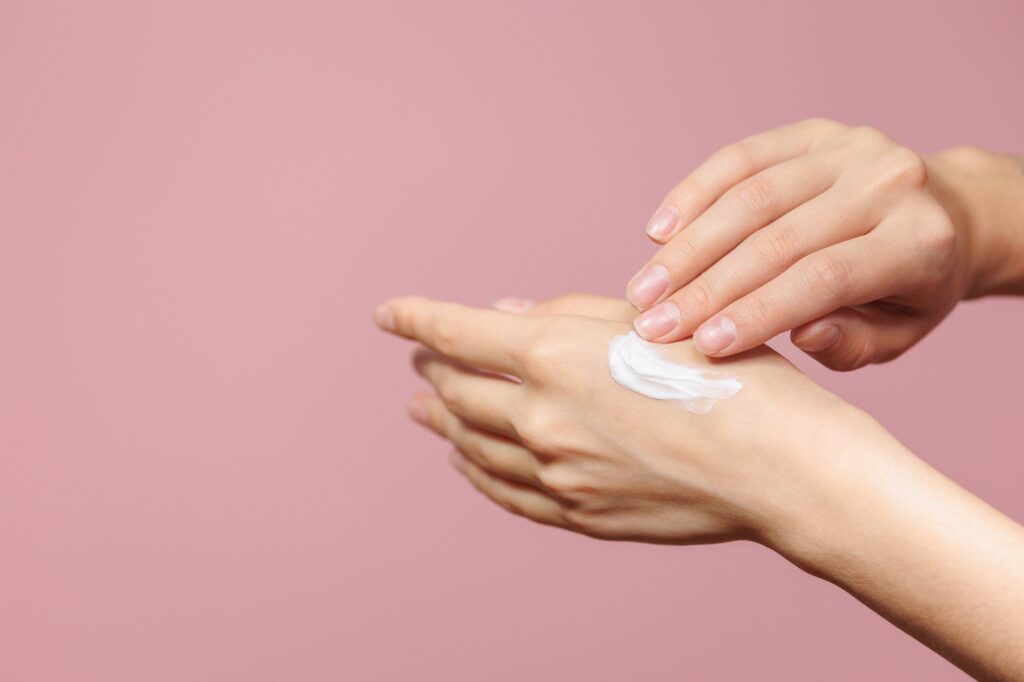 women's hands with cream or lotion on a pink background. skin care and hand and skin health during